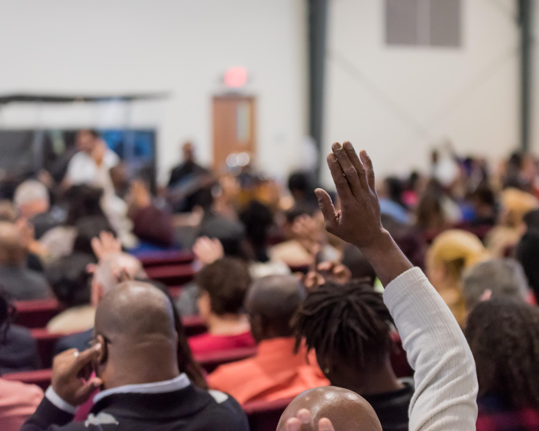 The Holy Temple congregation in worship with hands raised